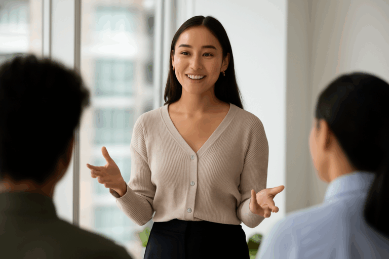 自信に満ちた表情で話す若い女性。柔らかな光が差し込むオフィスで、聞き手たちに向かって笑顔で語りかけている